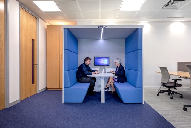 A man and a woman working on laptops within an acoustic booth 