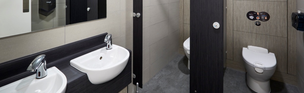 brown and beige toilet cubicles, 2 basins and mirror